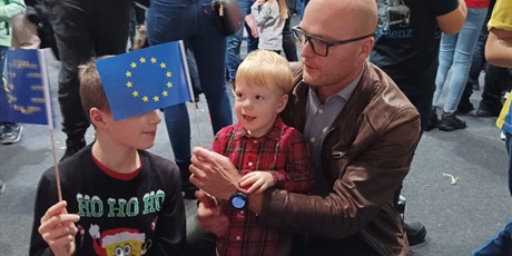 Powiększ grafikę: Mały chłopiec z tatą i bratem trzymają chorągiewkę Unii Europejskiej.