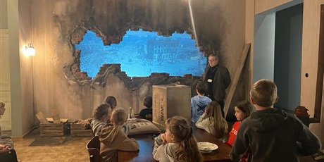 Powiększ grafikę: Dzieci z klasy 3b podczas lekcji warsztatowej w sali Muzeum stylizownej na pokój w kamienicy wojennej Warszawy po bombardowaniu. Wstawiona została ściana z dziurą po bombie.
