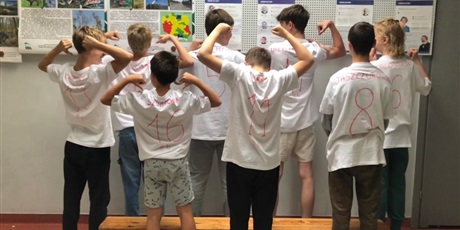 Powiększ grafikę: Chłopcy z 8b pozują tyłem do zdjęcia w koszulkach z napisanymi na plecach imonami chłopaków.