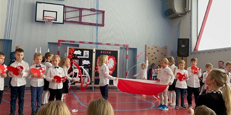 Powiększ grafikę: Dwoje dzieci z oddziału przedszkolnego stoi na środku sceny i trzyma flagę Polski, po bokach pozostałe dzieci trzymają czerwone serca.