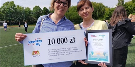 Powiększ grafikę: Dwie nauczycielki stoją na tle zieleni, trzymają bon na kwotę dziesięciu tysięcy złotych, wygrany w konkursie Rowerowy maj. 