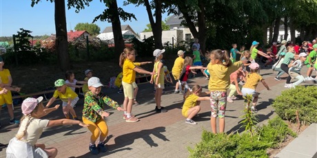 Powiększ grafikę: Dzieci ubrane na żółto robią przysiady na przed szkołą.