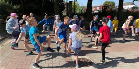 Powiększ grafikę: Dzieci ubrane na niebiesko robią rozgrzewkę na placu przed szkołą. Jeden chłopiec z prawej strony ubrany na czerwono-czarno.