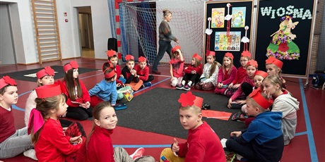 Powiększ grafikę: Grupa uczniów ubranych na czerwono siedzi w kole na podłodze.