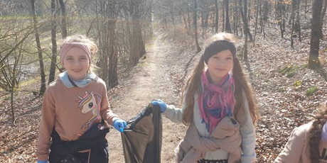 Powiększ grafikę: Dwie dziewczynki niosą wspólnie worek, w którym mają zebrane przez siebie śmieci.