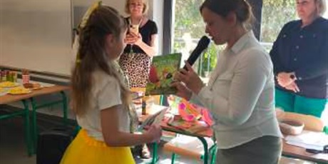 Powiększ grafikę: Dziewczynka w żółtej spódniczce i białej bluzce odbiera nagrodę w konkursie od Organizatorów konkursu Miejskiego konkursu recytatorskiego: Brzechwa - Przyjaciel dzieci.