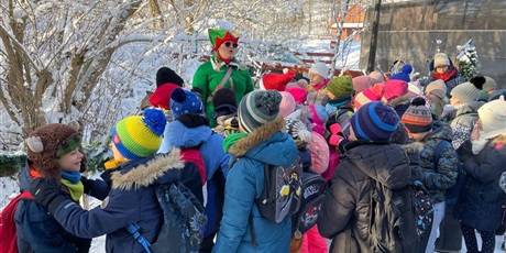 Powiększ grafikę: Uczniowie klasy 2b i 3b słuchają elfa na dworze u wejścia do Przystanku Świętego Mikołaja.