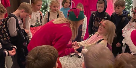 Powiększ grafikę: Uczniowie stoją w kole. W środku Pani Elf trzyma za ręcę dziewczynkę i coś do niej mówi.