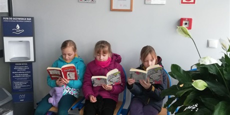 Powiększ grafikę: Trójka dzieci siedzi na ławce i czyta nowo zakupione przez Bibliotekę Szkolną książki.