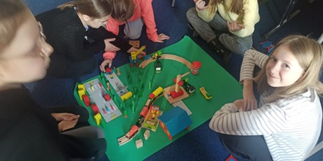 Powiększ grafikę: Dzieci budują ekoport na planszy papierowej z drewnianych klocków.