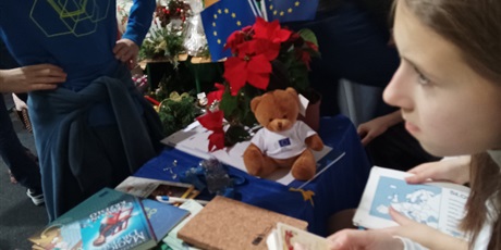 Powiększ grafikę: Stół nakryty granatowym obrusem w kolorach Unii Europejskiej. Na stole przy gwieździe betlejemskiej siedzi miś w koszulce Unii Europejskiej.