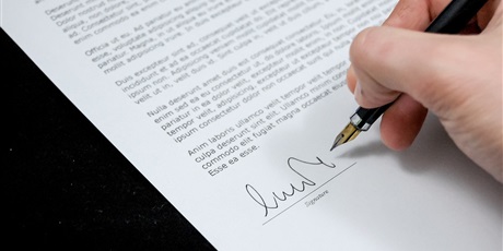 Powiększ grafikę: Umowa podpisywana przez rękę trzymającą pióro.
