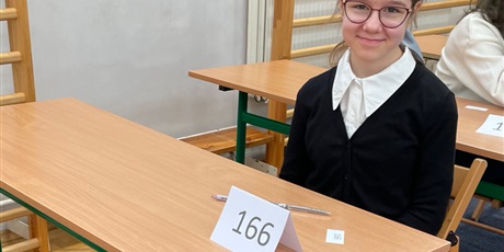 Powiększ grafikę: Uczennica siedzi przy sroliku na sali gimnastycznej i czeka na rozpoczęcie konkursu z biologii.