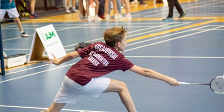 Powiększ grafikę: Uczeń z rakietą w prawej ręce odbija lotkę w badmintonie na boisku.