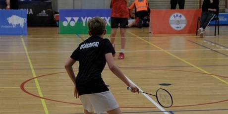 Powiększ grafikę: Uczeń na boisku stoi przygotowany do odbicia lotki w badmintonie.