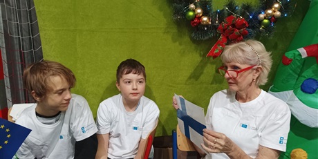 Powiększ grafikę: Pani Barbara Ignaciuk z dwoma chłopcami siedzi przy stoisku Unii Europejskiej.